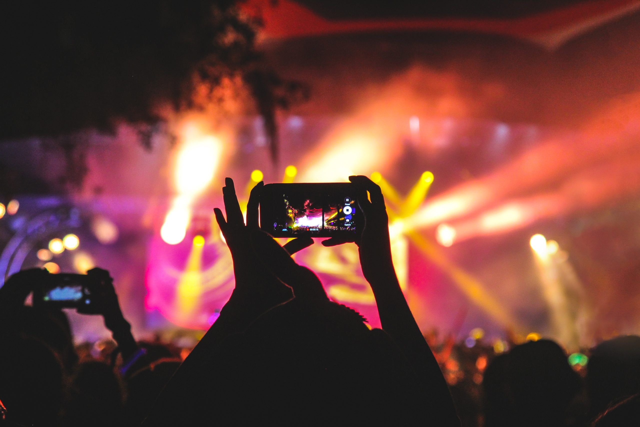 personne tenant un smartphone prenant une vidéo d'un concert près de la scène avec des lumières pendant la nuit